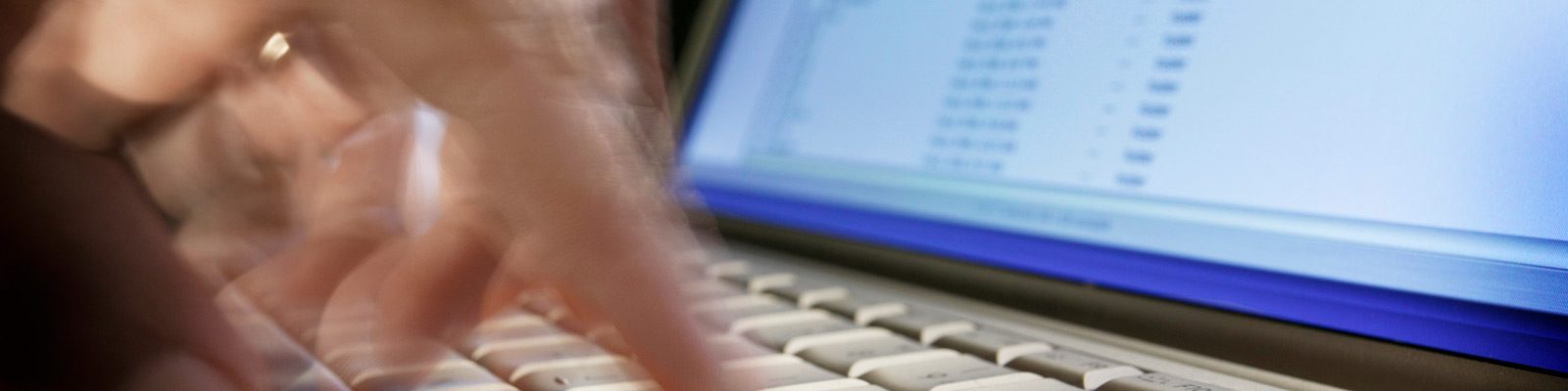 blurry image of ahand typing on a computer keyboard infront of a monitor.