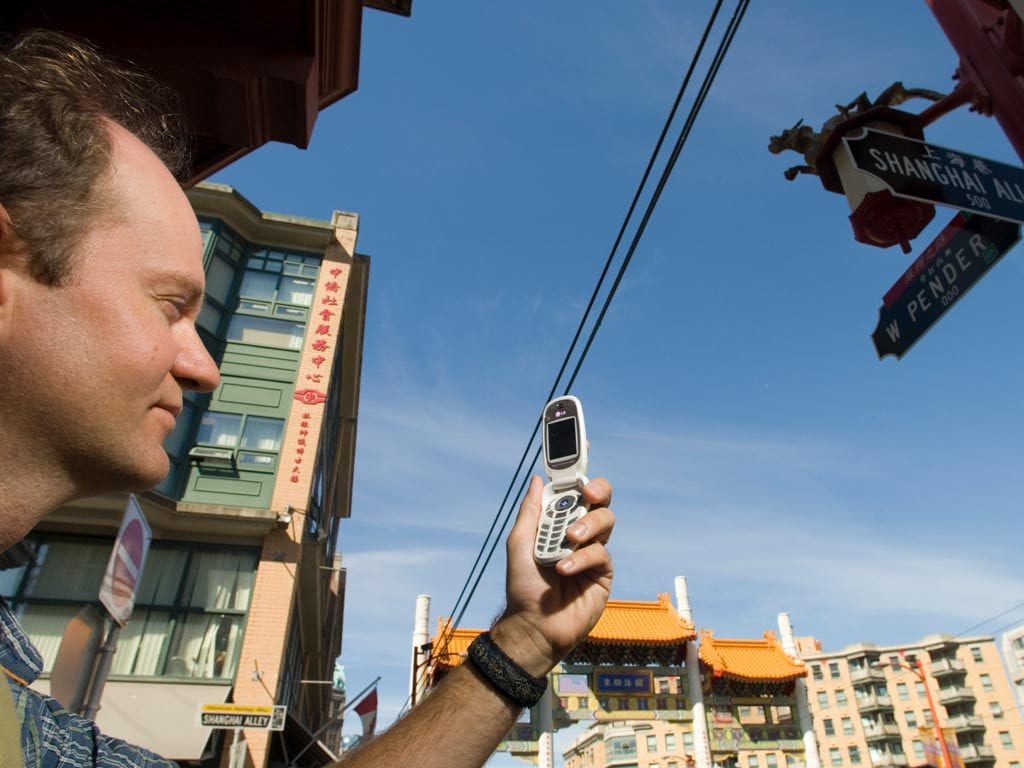 Man hlds looks at cellphone screen outside with buildingings and utility wires running
