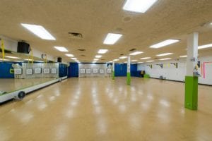 Activity room 2500 square feet that is well lit with fluorescent lights and one wall has mirrors with a beige floor.