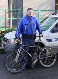 Security guard standing in front of a security vehicle with a bike in front of him.