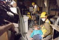 Disaster workers tending to injured person on ground.