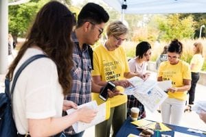 4 students under a patio display booth looking at papers.