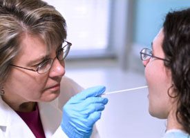 Medical person sticking thermometer into a person's mouth.