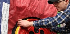 Male construction tradesperson with glasses in plaid shirt and baseball cap using a blower door tester.