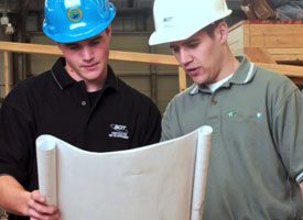 Two men with hard hats on looking at blueprints.