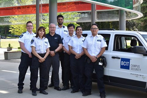 7 BCIT security staff posing in front of white security vehicle.