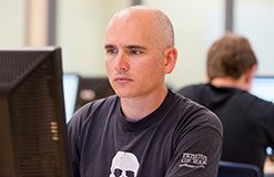 bald man with black t-shirt looking at a computer.