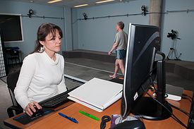Person sitting at computer and a person walking in the motion capture lab.