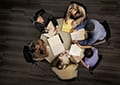 Photo looking down at a group of people meeting and sitting at a round table.