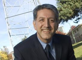 Photo of hassan farhangi wearing a black suit jacket, black tie and light blue shirt.