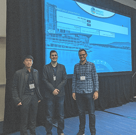 Photo of three people standing in front of a projector screen.