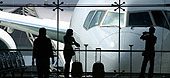 people in airport looking out the window at a parked jet.