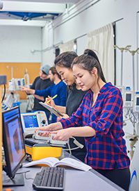 Photo of four students in biomedical engineering and one student is testing a defibrillator machine.