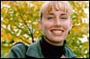 Photo of person standing in front of a tree wearing a green jacket over a black turtle neck sweater.