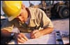 Photo of person wearing a yellow hard hat looking at plans.
