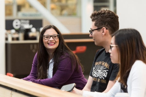Three students sitting in the BCIT atrium, smiling.