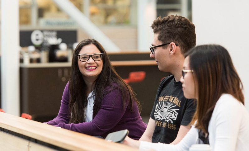 Three students sitting in the BCIT atrium, smiling.