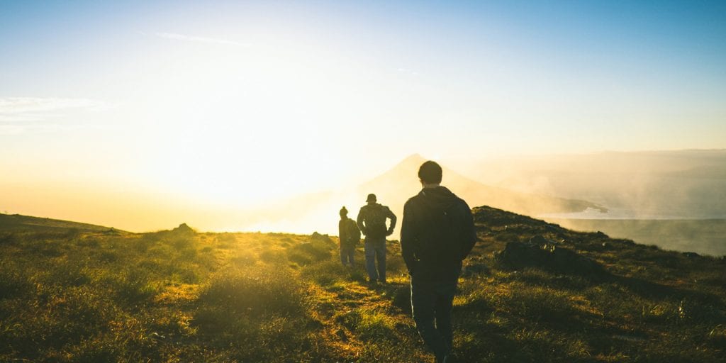 Hikers walking towards the sun in the grassy countryside.