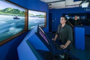Indigenous female student stands in front of marine instrument training panel, watching the virtual screen.