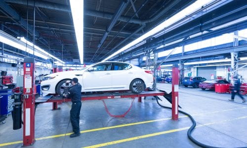 A student works on a white sedan raised on hoists