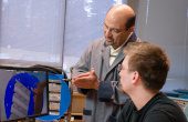 teacher pointing to machine parts with student looking on