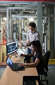 two students working on computers surrounded by pipes