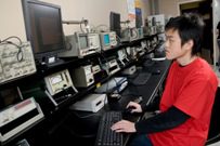 student in red t-shirt of asian decent using a computer-like machine