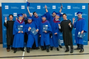 Two TMGT faculty members pose in front of a blue and white backdrop featuring the BCIT logo with seven TMGT BTech graduates at the March 2023 Convocation ceremony.