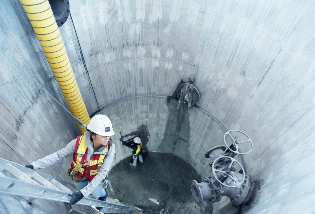 A female civil engineering student inspects a sewer junction pipe.