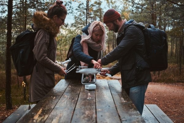 Two young women and a man assembling drone at a wooden table in the forest