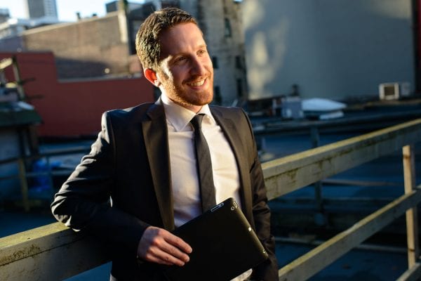 Man in suit and tie, smiling and holding a digital device.