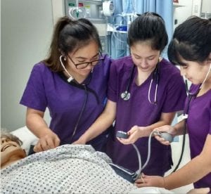 Three nursing students work with a patient simulator