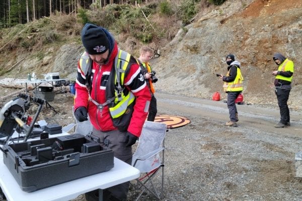 Four men in yellow vests setting up a drone on the road in a forested area