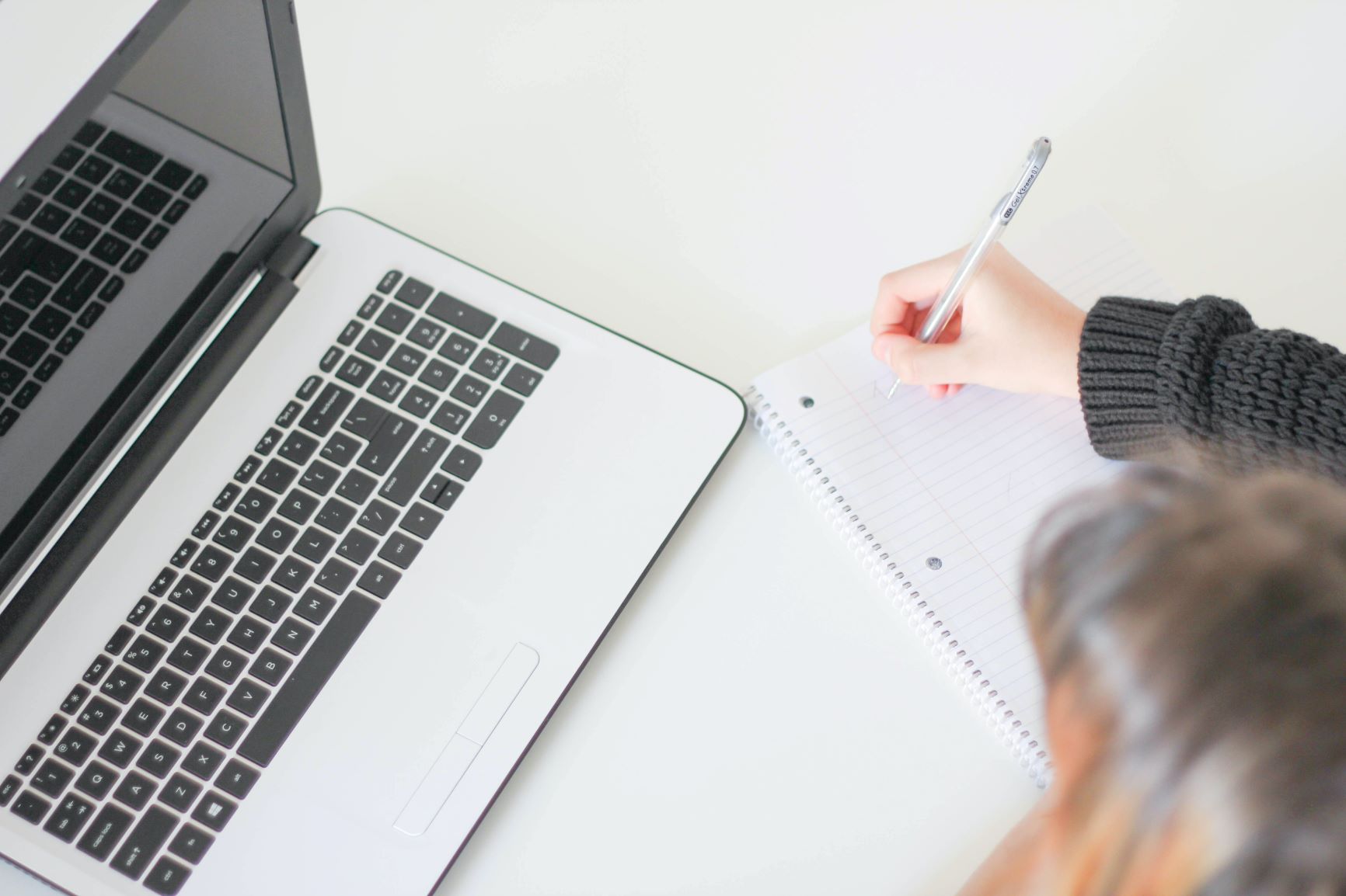 Person taking notes and looking at a laptop