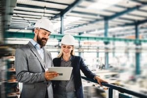 A portrait of a mature industrial man and woman engineer with tablet in a factory, working.