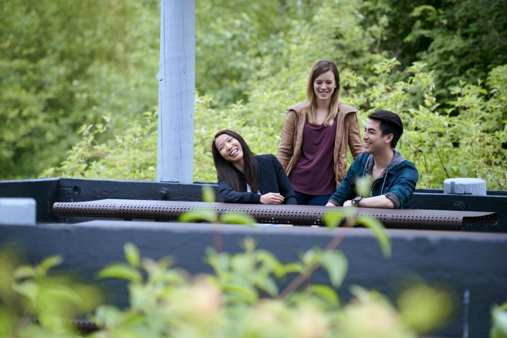 three students sitting in the forest who are enjoying themselves in conversation