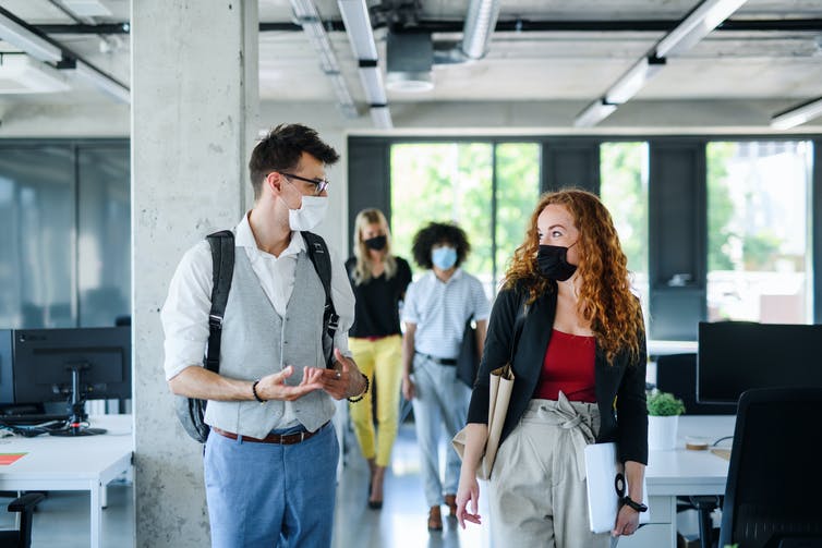 a male with a bag pack wearing glasses and a grey cardigan and a medical face mask who is speaking with a female student with a bag pack wearing a face mask and a red shirt