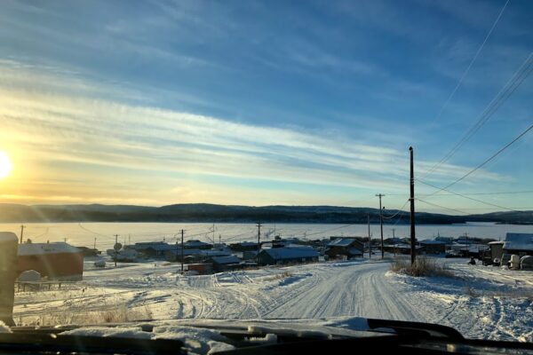 image of a First Nations community with blue skies, mountains and body of water in the background, and snow on the ground.