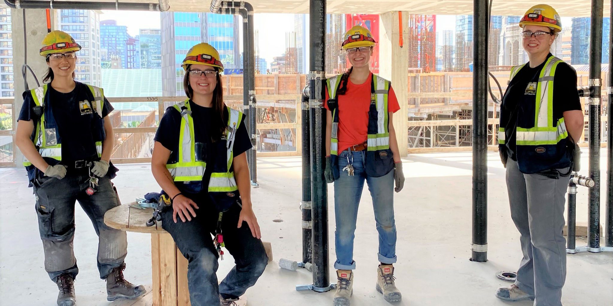 Four women standing in a construction site wearing hi vis vests and hard hats