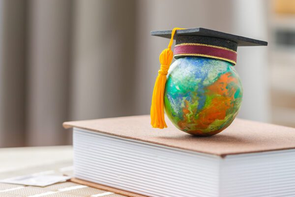 A globe with a graduation cap on top is on a book which is on a table