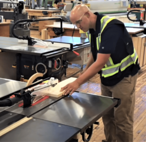 bald man working at a table saw in hi vis vest