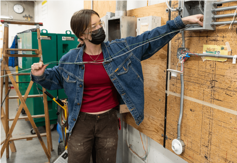 woman in red shirt and jean jacket doing electrical work