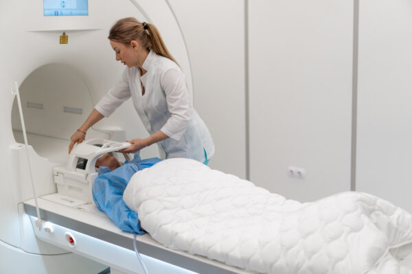 A MRI technolologist in a medical clinic puts the device on the patient's head before the brain magnetic resonance imaging procedure