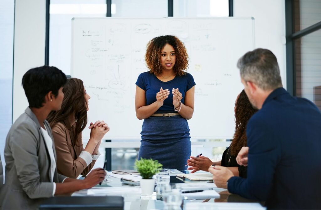 Woman with curly hair presenting to her colleagues in a board room