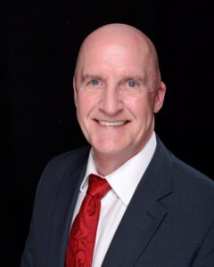 Chest-up portrait shot of Brian Hosier wearing dark suit, white shirt and red tie