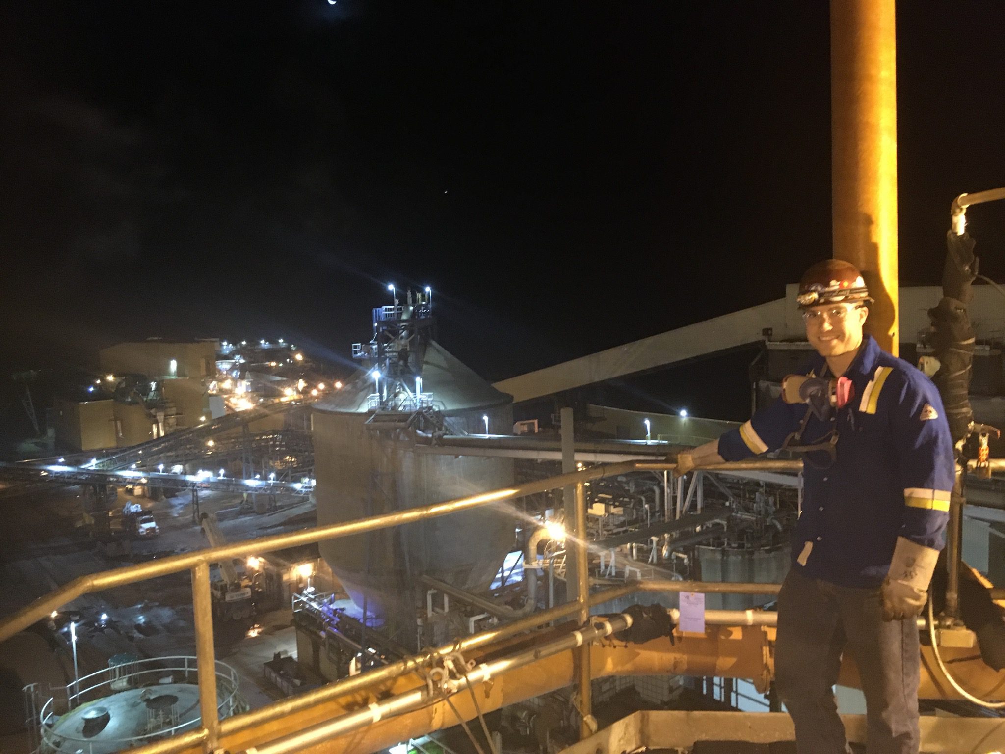 man in hard hat and safety glasses stands at railing overlooking a piping yard