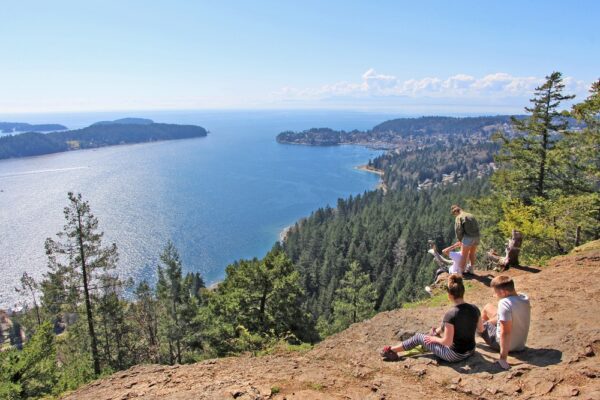 Soames Hill park in Sunshine Coast, BC. The view on the 2 couple sitting and resting on the hill with the aerial view on Gibsons surrounded by forest / woods and ocean.