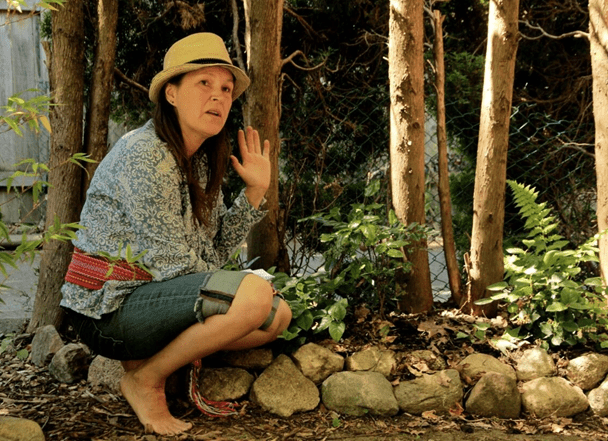 women crouched in front of rocks and trees with her hand up