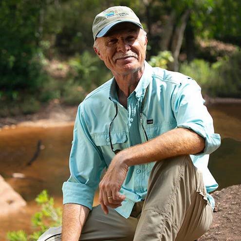man in blue button down and grey hat sitting in front of a river