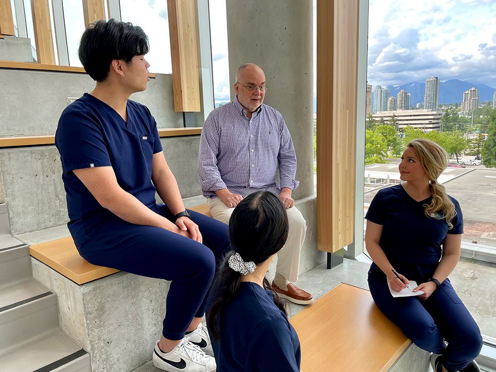 patient partner Bill sitting on stairs with 3 health sciences students